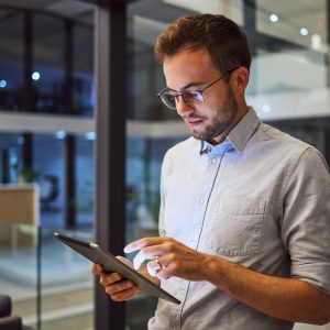 Man in office, working on tablet at night in the office and testing campaign strategy for marketing