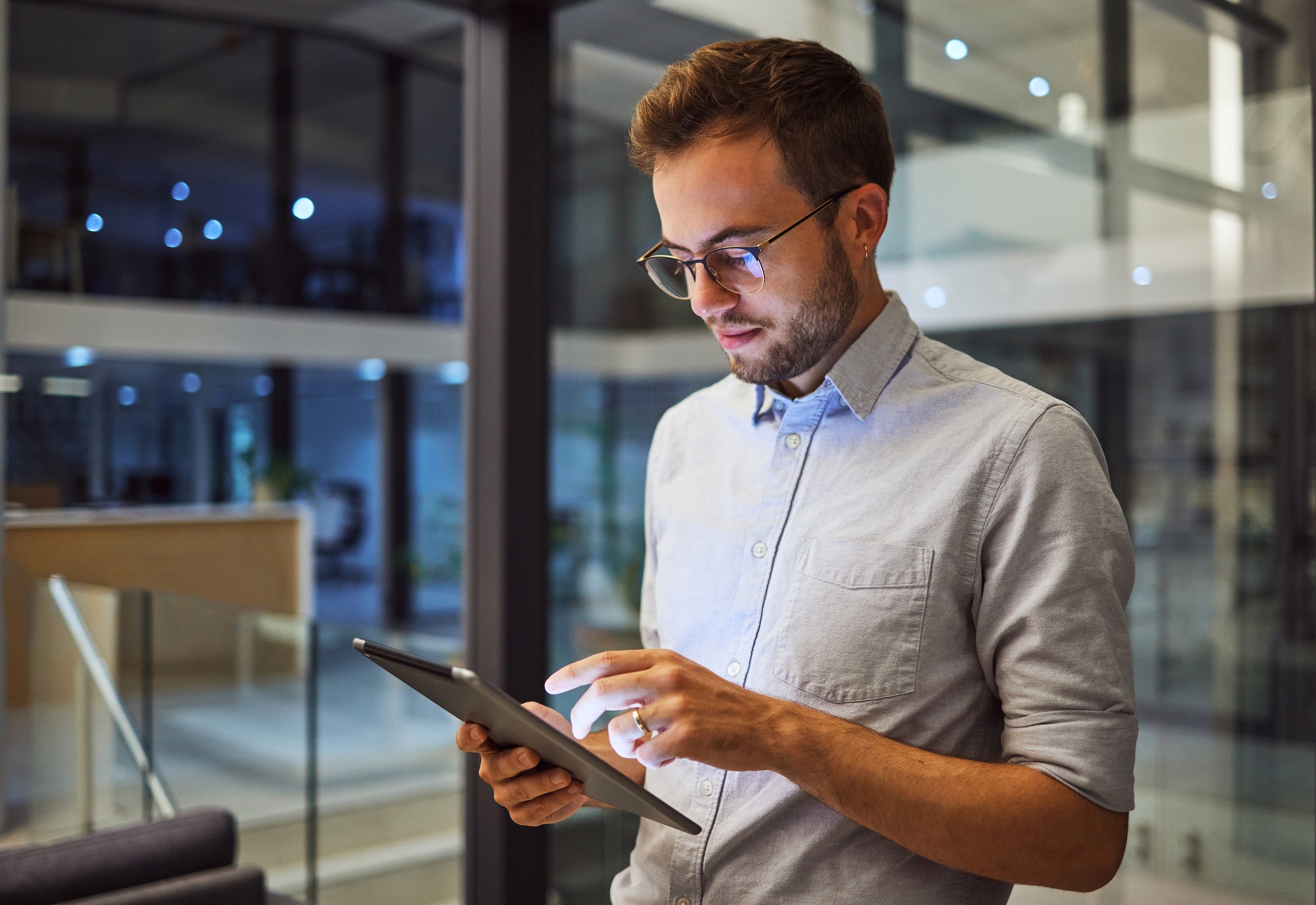 Man in office, working on tablet at night in the office and testing campaign strategy for marketing